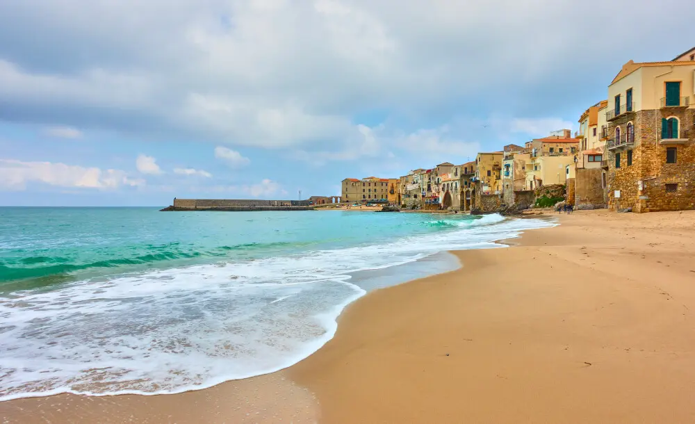 Spiaggia sabbiosa, onde, case colorate sul mare.