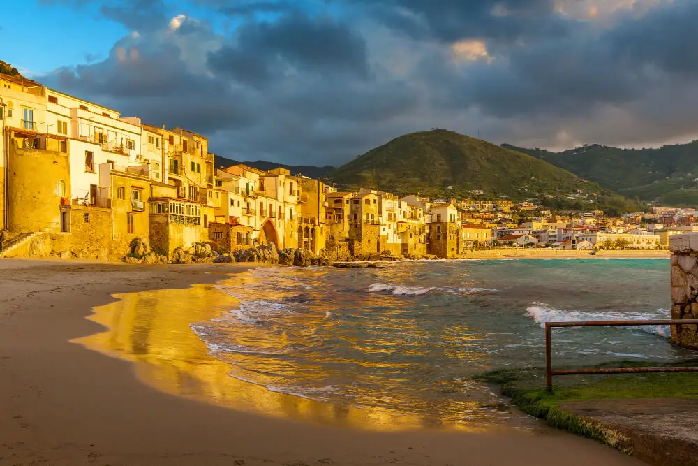 Città costiera al tramonto, case color oro, mare dorato.