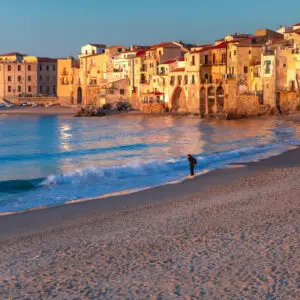 Spiaggia sabbiosa, mare azzurro, borgo antico al tramonto.