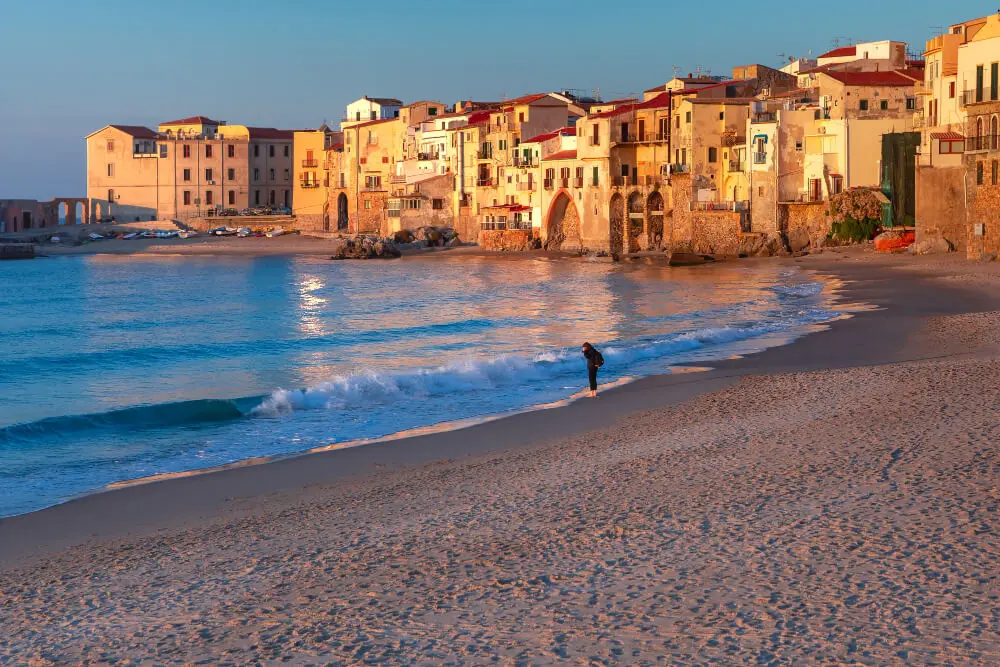 Spiaggia sabbiosa, mare azzurro, borgo antico al tramonto.