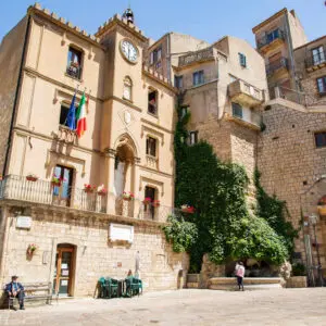 Municipio storico, piazza in pietra, vegetazione lussureggiante.