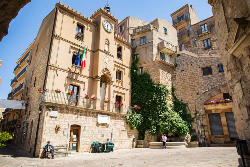 Municipio storico, piazza in pietra, vegetazione lussureggiante.