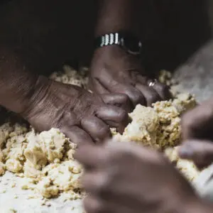 Mani che impastano pasta gialla su superficie di legno.