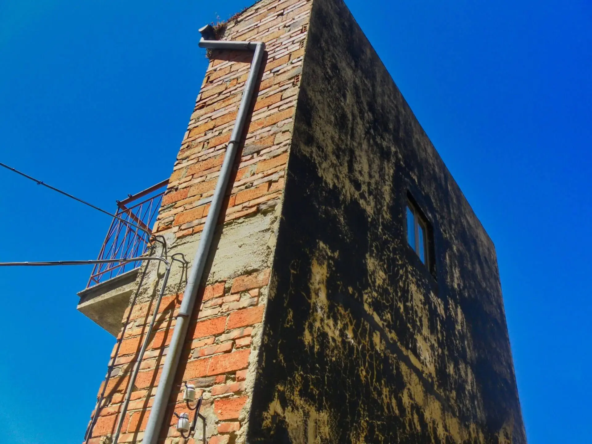 Edificio angolare in mattoni, grondaia, piccolo balcone, cielo blu.