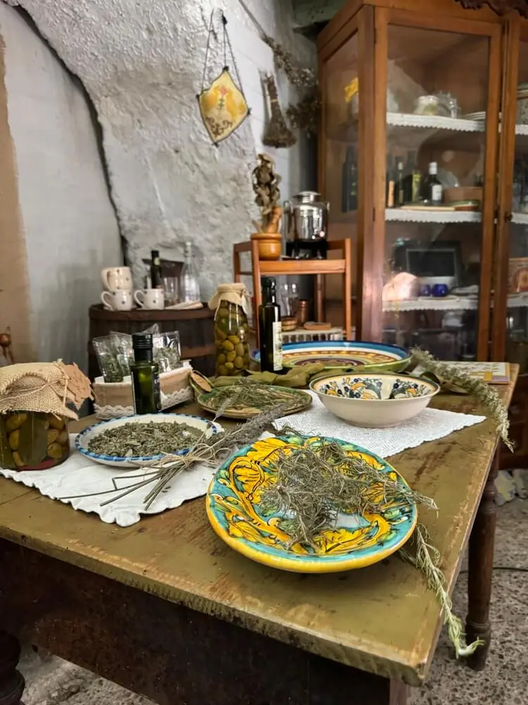 Tavolo rustico con erbe, olive e ceramiche dipinte a mano.