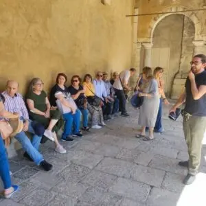 Gruppo di persone sedute e in piedi in cortile antico.