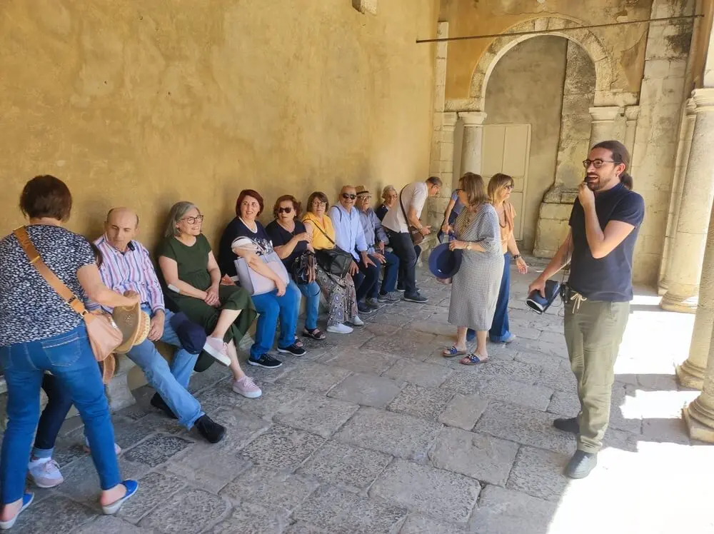 Gruppo di persone sedute e in piedi in cortile antico.