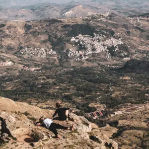 Due persone riposano su una scogliera, vista panoramica di un paese.