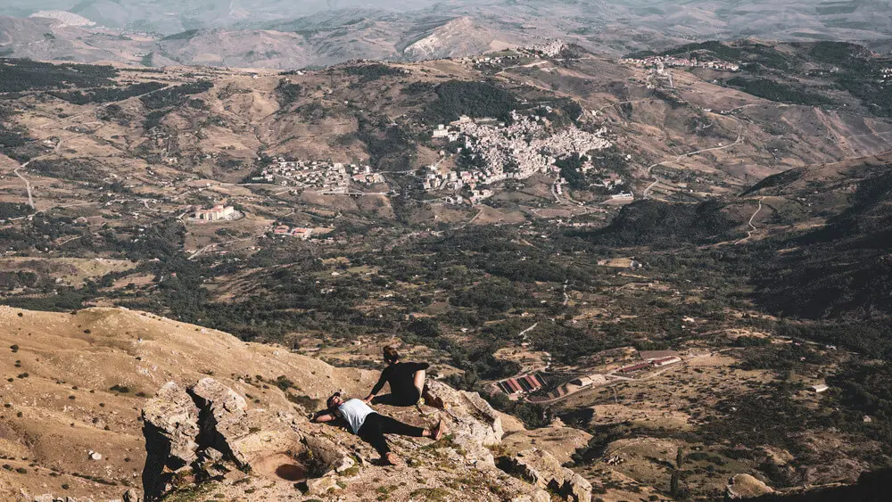 Due persone riposano su una scogliera, vista panoramica di un paese.