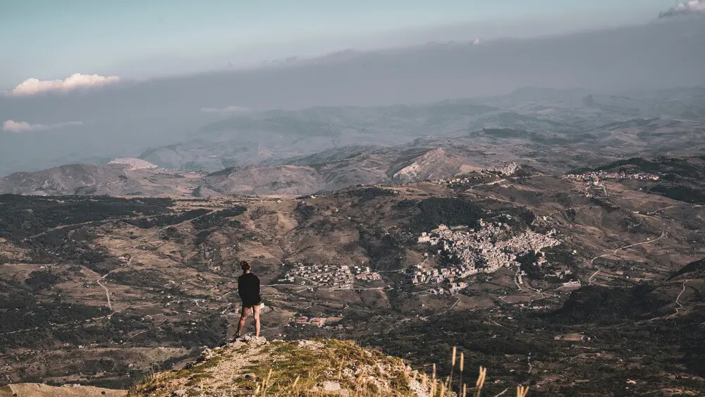 Persona ammira paesaggio montano, vasto e un villaggio in lontananza.