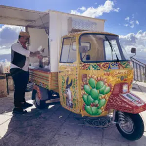Chiosco ambulante siciliano dipinto, venditore prepara cibo.