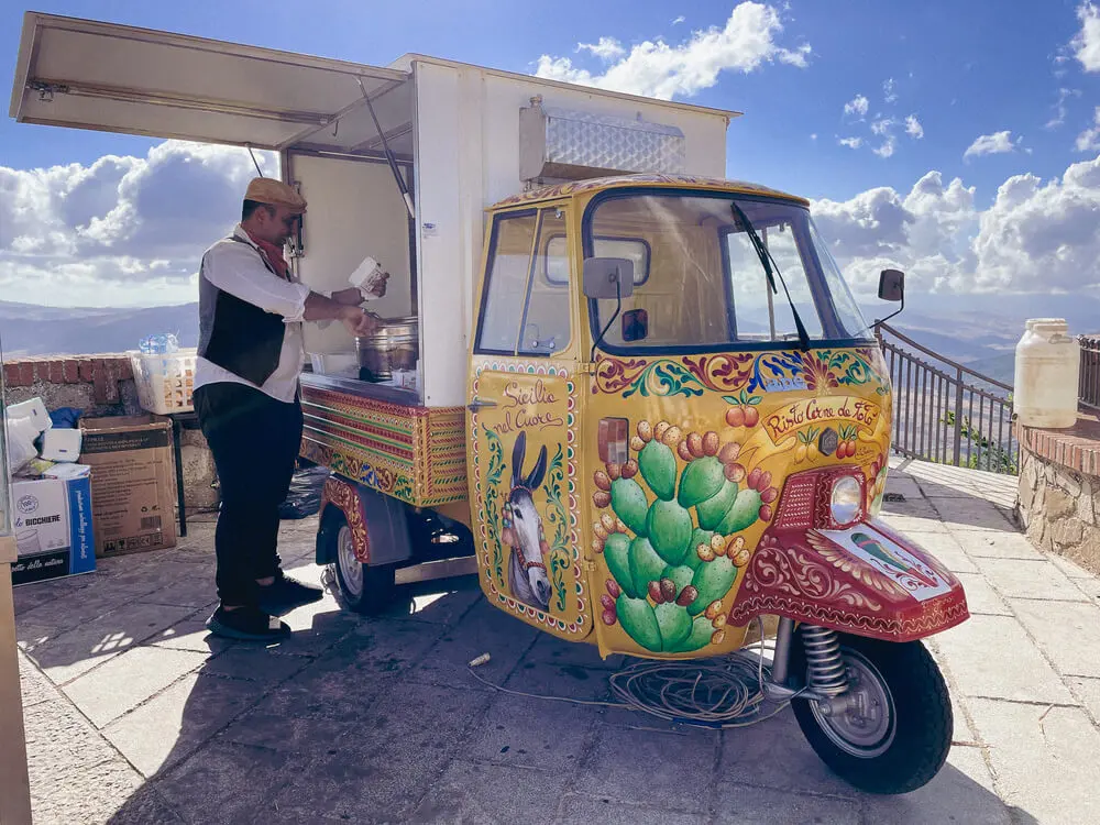 Chiosco ambulante siciliano dipinto, venditore prepara cibo.