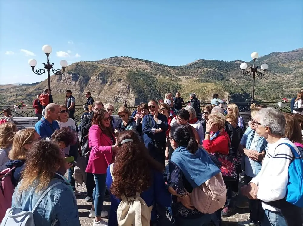 Grande gruppo di persone ammira un panorama collinare.