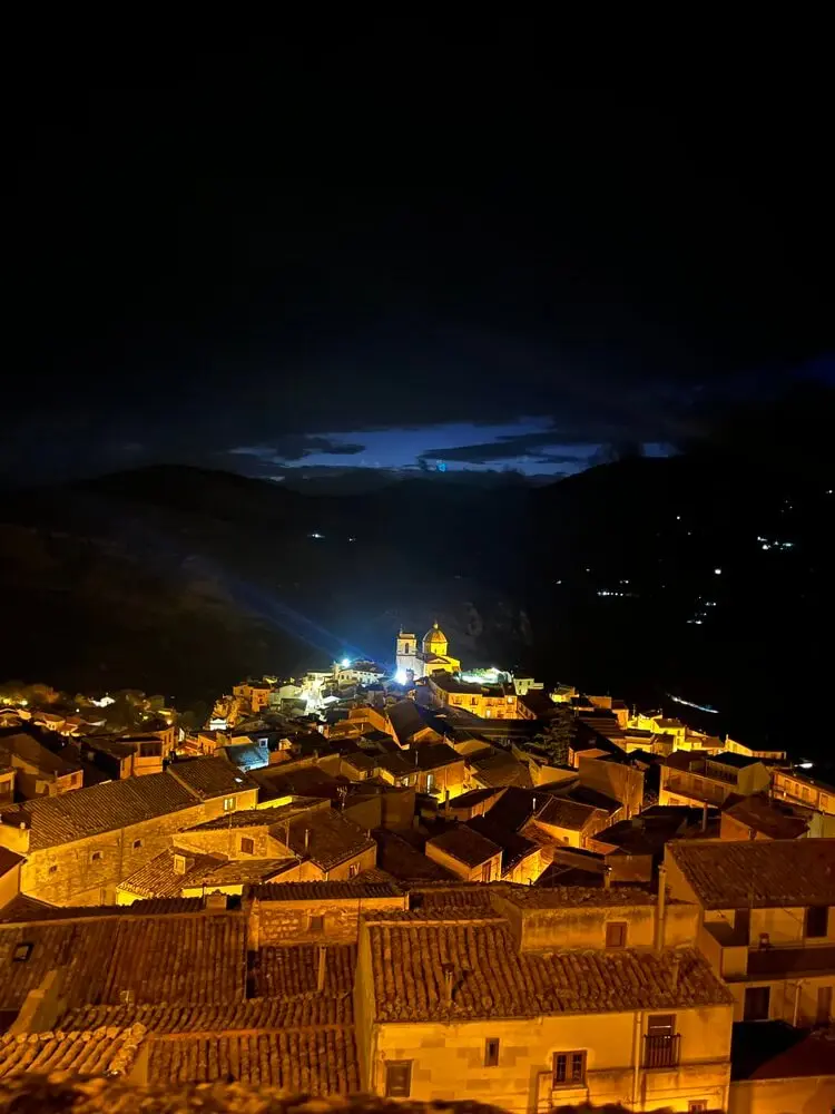 Paesino illuminato di notte, sullo sfondo montagne.