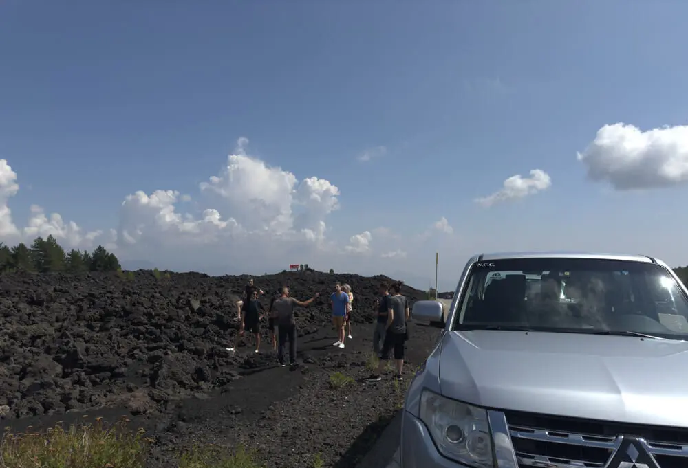 Gruppo di persone su campo lavico, auto in primo piano.