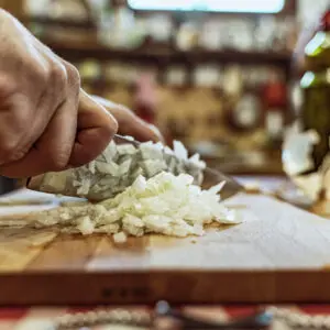 Mani che tritano cipolla bianca su tagliere.