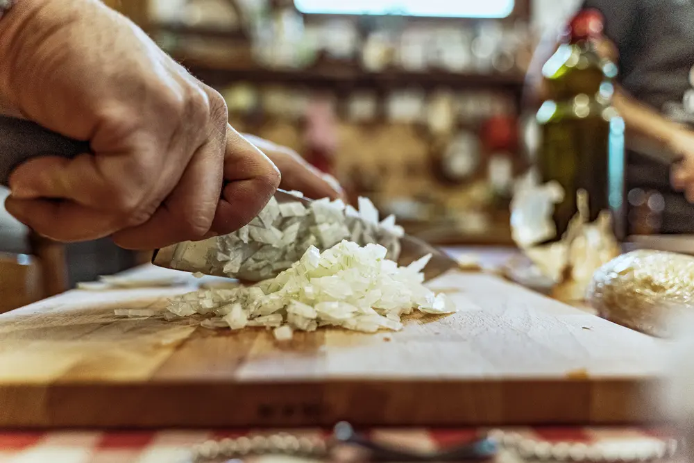 Mani che tritano cipolla bianca su tagliere.